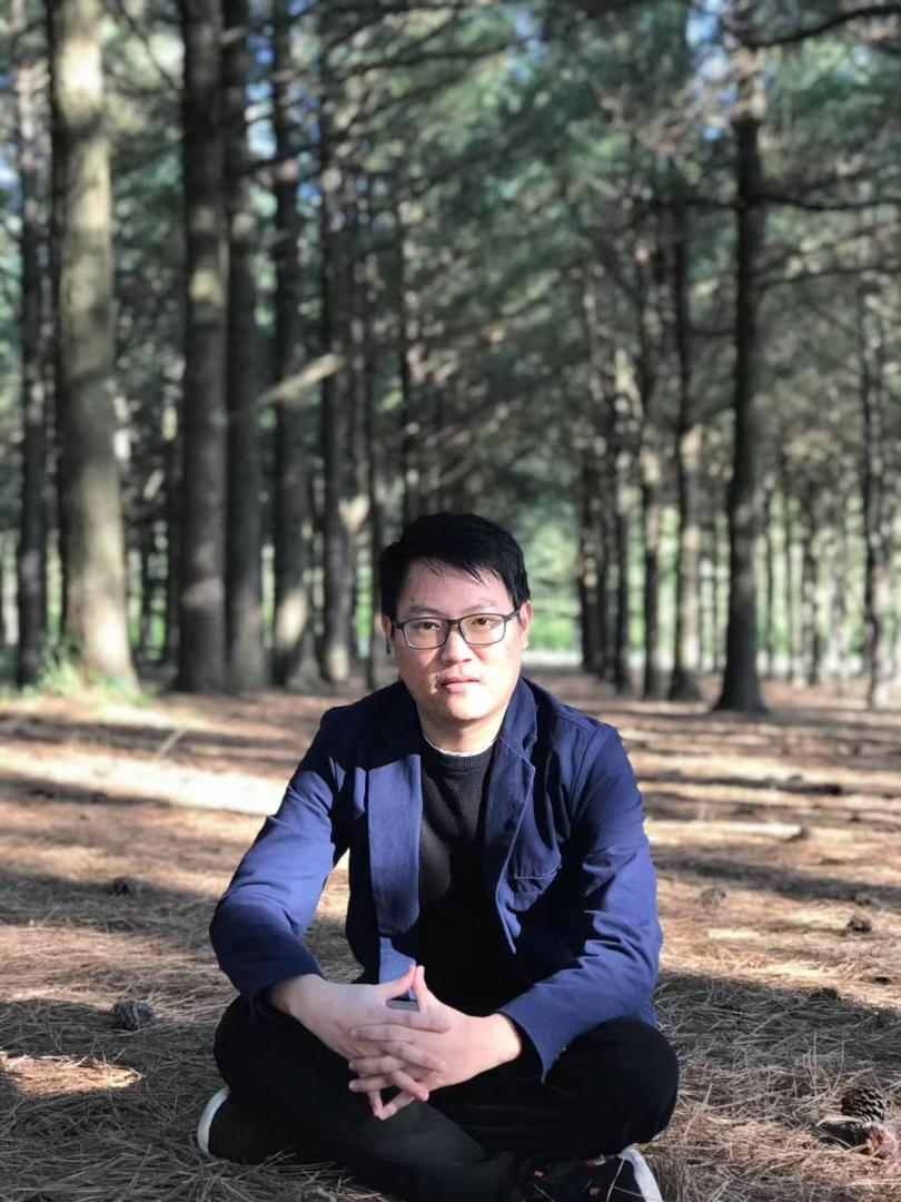 Photo of doctoral candidate Xiaojin Wang sitting in a wooded area.